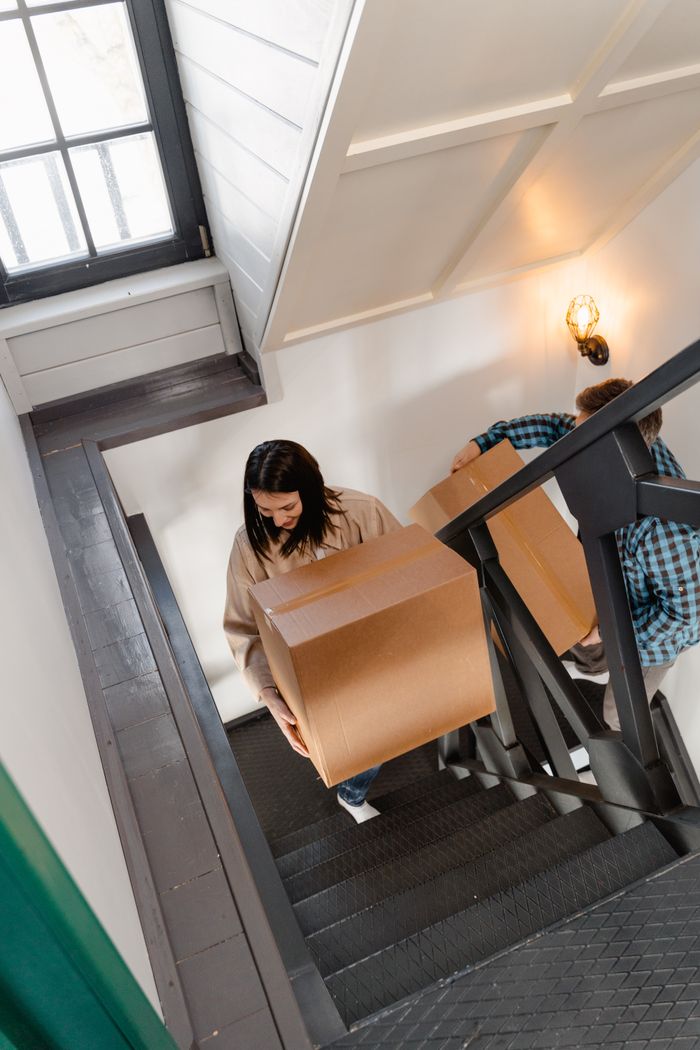 gallery-5 A couple carrying large boxes up a stairway in their new home, symbolizing a fresh start.