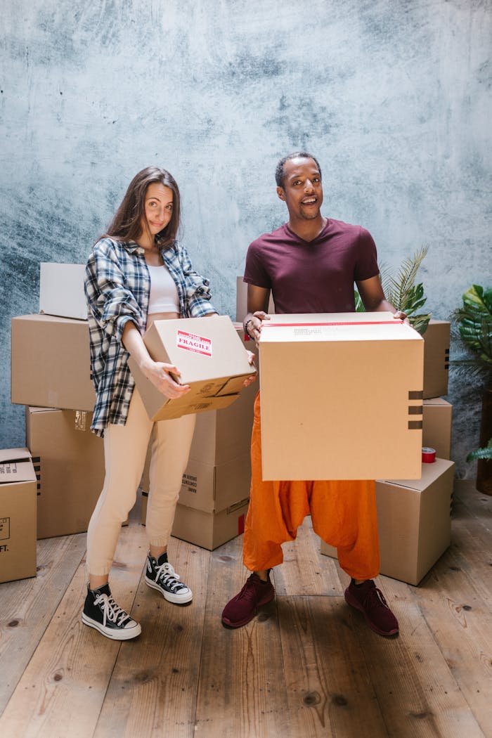 services-01 Two young adults smiling while moving boxes into a new home.